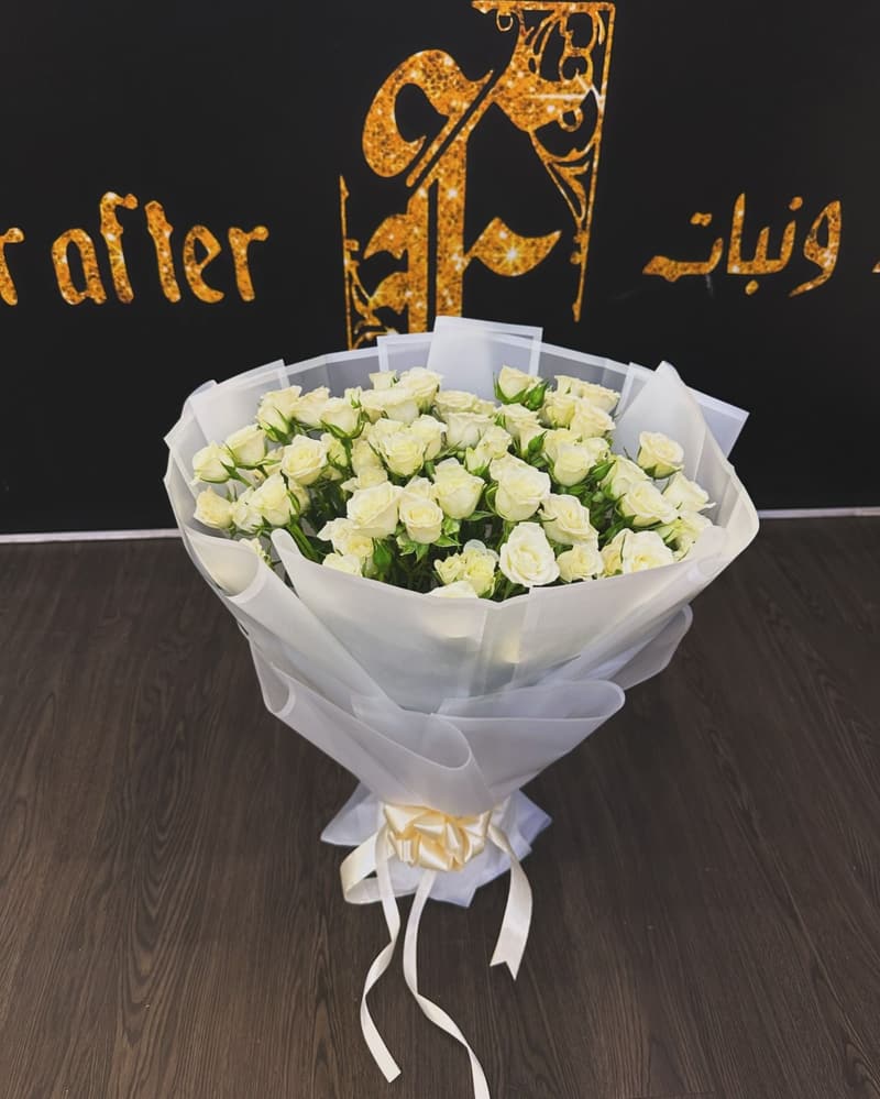 بوكيه ورد أبيض بتغليف أبيض أمام جدار الشعار الذهبي في المحل