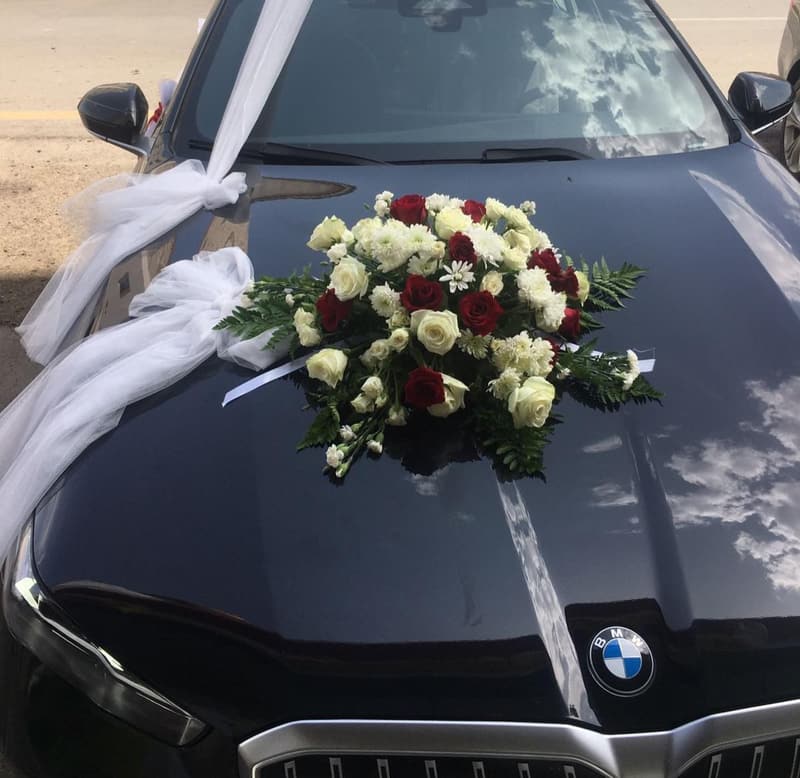باقة ورد أبيض وأحمر مع شرائط تُل على غطاء محرّك سيارة سوداء