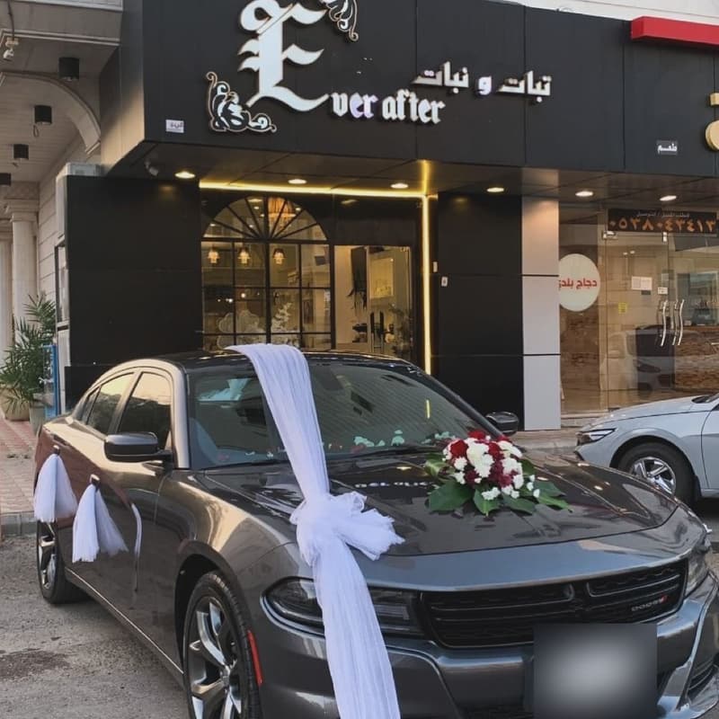 سيارة زفّة مزيّنة بالتُّل الأبيض وباقة ورد أمام واجهة محل تبات ونبات